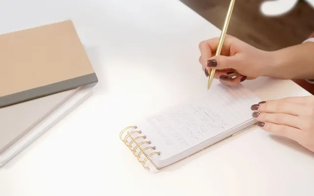 Hai bàn tay đang ghi chép vào sổ tay trên bàn làm việc
