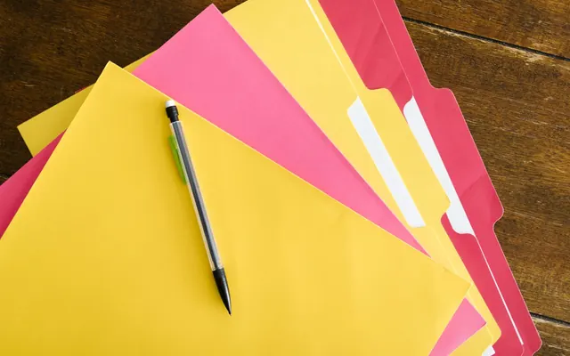 Các tập hồ sơ nhiều màu và một chiếc bút chì trên mặt bàn gỗ